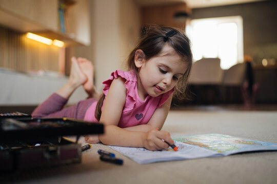 young girl sketches with crayons, young girl concentrates on colorful drawing near backpack in cozy room