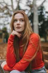 autumn woman pondering, young woman sitting on park bench surrounded by autumnal colors and gentle...