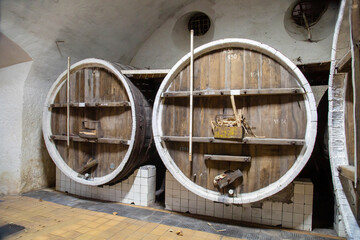 Large wooden oak barrels standing in the tunnel of the winery. Winemaking viticulture wine blend.