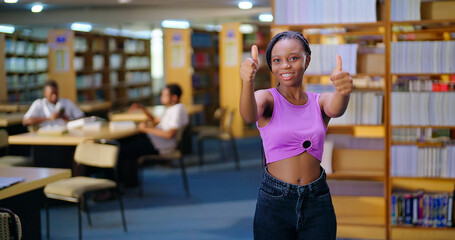 African young adult gen z happy student indoor library look camera show thumbs up hand sign ready for exam smiling girl staring cam do pose enjoy day time inside college