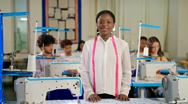 African happy smiling young adult gen z lady woman wear tape around neck staring camera class room. Teen pupil girl look cam do casual pose learn new sewing craft skill course indoor day college place