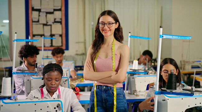 Indian young adult gen z happy female wear glass tape around neck staring camera cross arm class room learn sewing craft course skill. Teen girl look cam fold hand do casual pose new day indoor place