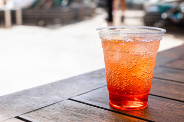 A refreshing drink in a clear plastic cup filled with sparkling orange soda. The cup is placed on a wooden table with a blurred background.