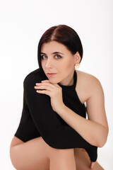 Young woman in black bodysuit posing sitting isolated on white background.