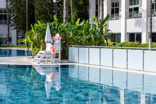 A clear swimming pool with a lifeguard chair and a buoy. Lush green plants surround the area. The scene is bright and inviting, perfect for relaxation.