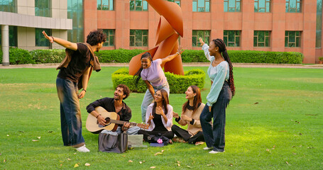 Indian young adult gen z male man hold guitar play new music lady woman sing song have fun joy. Happy pupil girl boy guy group spend day break time do funny dance enjoy relax mood at garden park place