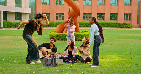 Indian young adult gen z male man hold guitar play new music lady woman sing song have fun joy Happy friend girl boy guy group spend day break time do funny dance enjoy relax mood at garden park place