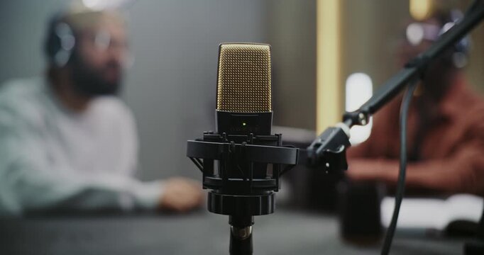 Close Up of Professional Condenser Microphone, Provides Audio Technology, High Quality Sound. Two Men Blurred in Background, Conducting Podcast or Interview. Creative Exchange in Modern Media Space.