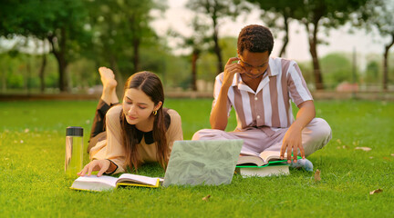 Indian young adult gen z lady female lying on grass use laptop look screen check new email e work garden park. Busy pupil male man do exam study read course book spend break time day college place