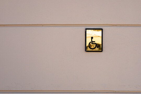 A golden wheelchair symbol mounted on a light-colored wall. The sign indicates accessibility for individuals with disabilities.