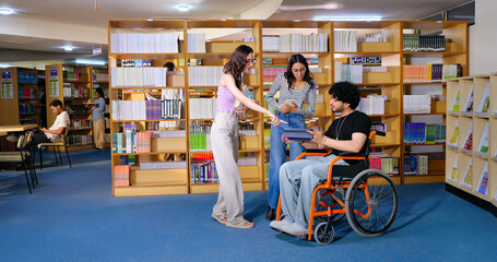 Indian young adult male man sitting wheel chair use tablet take part group study speak show screen share new ideas indoor gen z pupil teen girl boy hold book talk library college place © Raushan_films