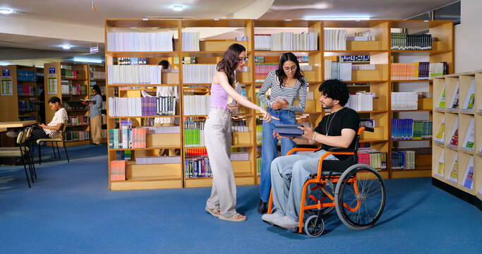 Indian young adult male man sitting wheel chair use tablet take part group study speak show screen share new ideas indoor gen z pupil teen girl boy hold book talk library college place