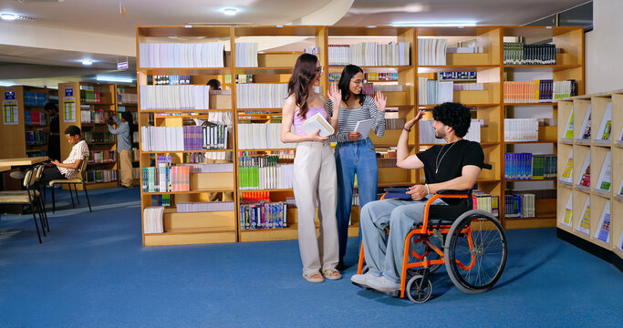 Indian young adult man sitting wheel chair hold tablet book take part group study speak share new ideas indoor gen z pupil teen girl boy talk do greet say hello library college place