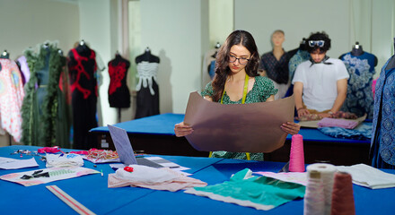 Indian young adult gen z female lady wear tape around neck learn clothe craft skill indoor class room girl use laptop look screen typing hold paper do fabric work look pattern new day college place