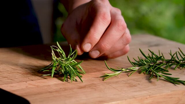 Horizontal close-up of fresh rosemary being stripped by hand and then chopped on a cutting board. Clear view of texture, preparation steps, and natural kitchen workflow.