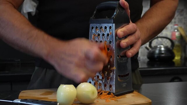 A man and her daily household chores. A man is cooking in the kitchen. A man is peeling onions and grating carrots.