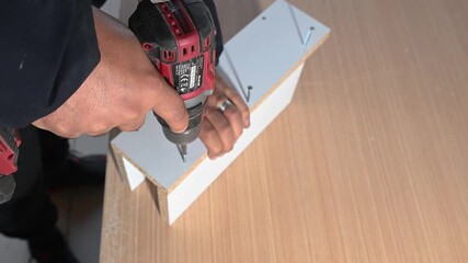 The carpenter is tightening screws in a piece of furniture with a cordless drill. Furniture assembly, carpentry, and a do-it-yourself (DIY) project.