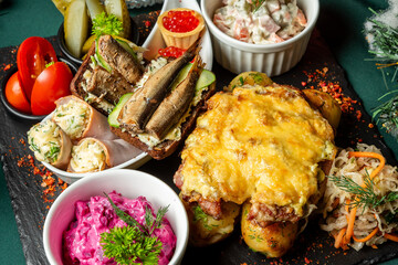  A traditional Eastern European holiday meal featuring a festive assortment of dishes, including sprat sandwiches, Olivier salad, beet salad, and cheesy baked potatoes on a dark table