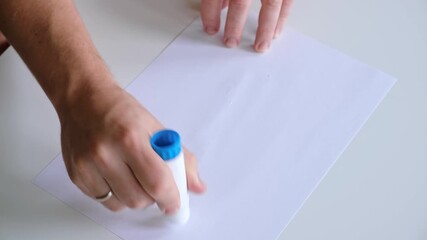 A man's hand smears a white paper sheet with a glue stick. A teacher of a creative profession. A DIY handmade lesson. High quality 4K footage.