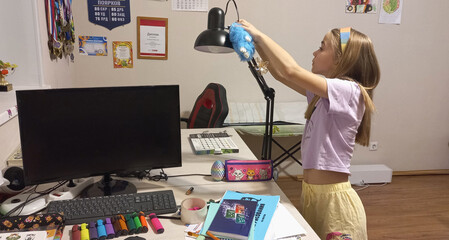 Young girl adjusting desk lamp while studying in home office  