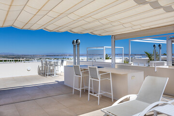 Fototapeta premium Rooftop terrace with sea view, bar seating, and sun loungers under canopy