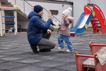 Father and daughter creating a high five on a playground, sharing a cheerful moment outside