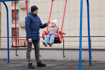 Father and daughter enjoying time together on a playground swing during winter