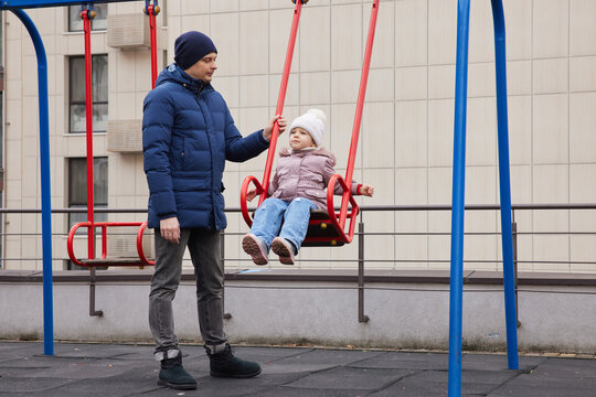 Father and daughter enjoying time together on a playground swing during winter - Powered by Adobe