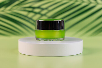 Jar of cosmetic cream on a white round shaped podium against light green background with soft shadow of leaves