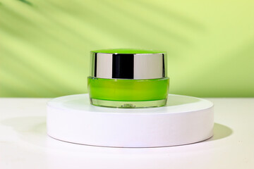 Jar of cosmetic cream on a white round shaped podium against light green background with soft shadow of leaves