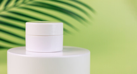 white Jar of cosmetic cream on a white round shaped podium against light green background with soft shadow of leaves and copy space