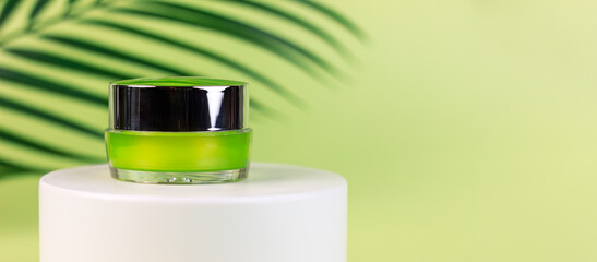 Jar of cosmetic cream on a white round shaped podium against light green background with soft shadow of leaves and copy space