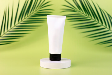 empty white cream tube on a white square shaped podium against light green background. cosmetic mockup display