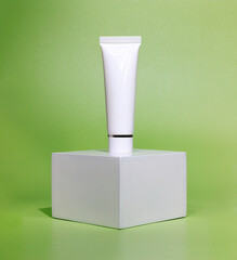 empty white cream tube on a white square shaped podium against light green background. cosmetic mockup display