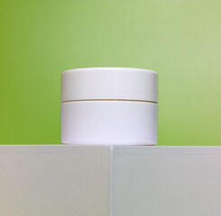 close up of empty white Jar of cosmetic cream on a white square shaped podium against light green background. cosmetic mockup display