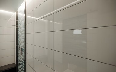 Sleek modern bathroom interior featuring a wall of large glossy white tiles with elegant recessed lighting