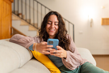Woman relaxing on sofa browsing smartphone smiling