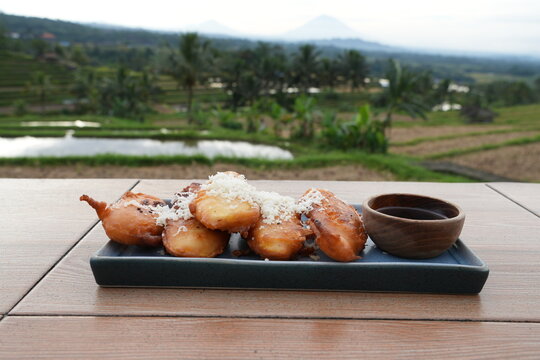 Delicious fried banana on rectangle ceramic plate on the table with palm sugar sauce. Rice field background. Tabanan, Bali, Indonesia, July 3 2025