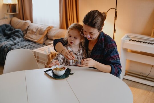 A young mother lovingly feeds her 4-year-old daughter porridge, capturing a natural morning routine of care and family bonding. Authentic parenting moment - Powered by Adobe