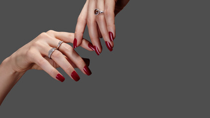 Close up of female hands with red gel polish manicure on nails and luxury rings. Timeless elegance for beauty salons, nail masters, and advertising of professional nail care and hand treatment