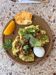 directly above shot of healthy meal, smashed avocado 
with spiced almonds, herb salad and a soft boiled egg on sourdough with halloumi