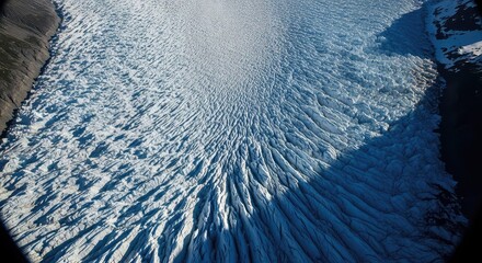 Aerial view of a massive glacier with intricate ice patterns and crevasses flowing through a valley.