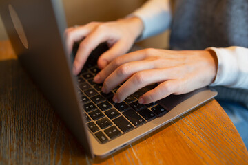 Closeup of hands typing on a laptop keyboard at a wooden table in a cafe. Concept remote work, productivity, freelancing.