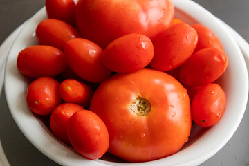 bunch of tomatoes and cherry tomatoes in a white bowl on dark background