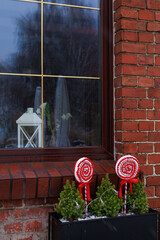 Window of a brick house with evergreen planter and red lollipop decorations. Concept of christmas decoration, retail display, postcard and winter design.