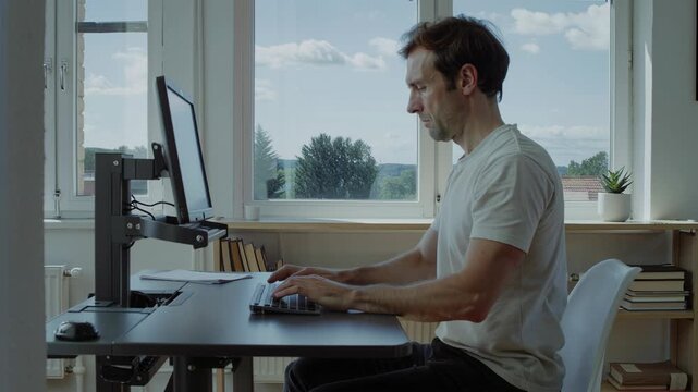 Man typing on keyboard at a comfortable ergonomic desk setup during work from home. Remote work productivity with natural window light.