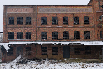 Snow-covered facade of an abandoned brick factory with a collapsed roof section. Concept of industrial decline, historical documentation and visual support for social or economic articles.