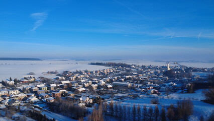 A serene aerial view of the village Hnevosice covered in fresh winter snow. Traditional houses, fields, and quiet streets form a peaceful rural landscape, surrounded by snow-covered trees and hill