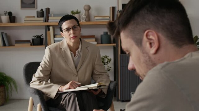 Rack focus view of millennial veteran soldier undertaking trauma-focused therapy session provided by mature psychotherapist in modern office