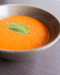 creamy roasted tomato and red pepper soup in black bowl with fresh basil
